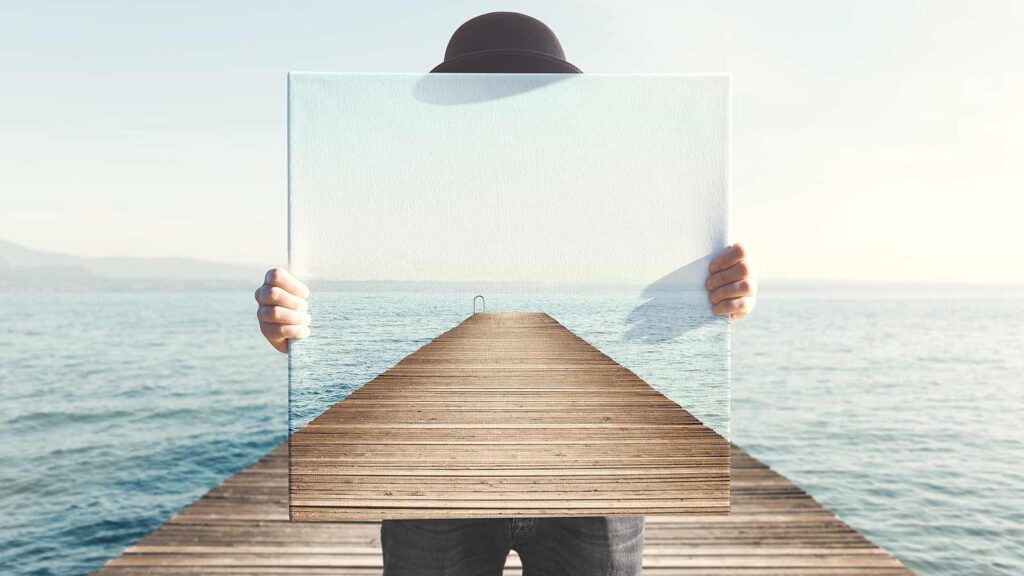 A person standing on a dock over the water holds a framed picture of the dock extending into the water, creating an optical illusion that resembles the layered perspectives often seen in market research.